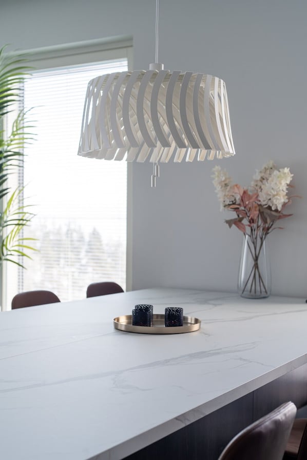A modern dining area with a white marble table, a decorative hanging light fixture, and a vase with flowers. - Luxurious Penthouse - Hot Tub & Sauna (Tampere)