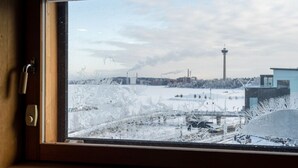 Una ventana con vista a un paisaje nevado, una torre y edificios industriales.