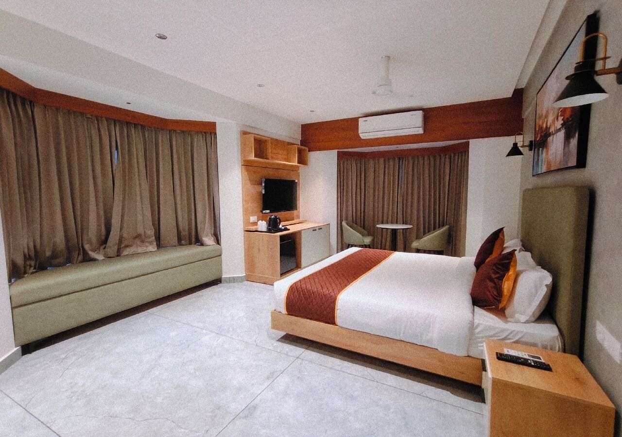 A hotel room with a bed, a desk, a chair, a small table, and a sofa.