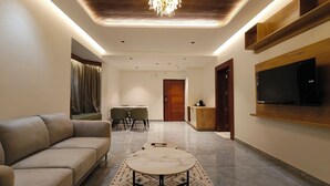 Un salon moderne comprenant un canapé, une table basse, un téléviseur fixé au mur et un coin repas avec des chaises et une table.