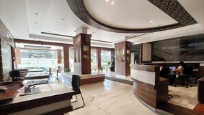 En moderne hotellobby med reception, siddeområde og trappe op til en etage.