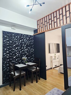 Ein modernes Zimmer mit Essbereich, ausgestattet mit einer raumteilerartigen Wand mit geometrischem Muster, einem Holztisch mit Stühlen und einer Deckenleuchte.
