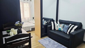 En kompakt opholdsstue med sofa, et lille bord med stearinlys og en lænestol.