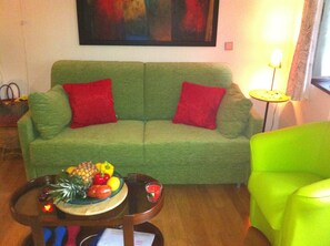 A green sofa with red cushions, a small wooden table with a fruit bowl, and a bright green armchair. - Green Nest in Paradise Colletta, Liguria, Italy, hiking, climbing, pool (Colletta di Castelbianco, Castelbianco)