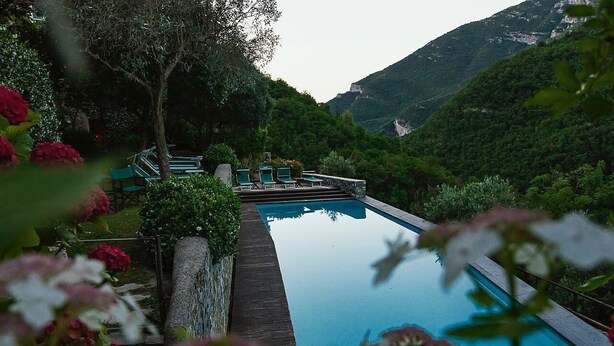 Un espace piscine doté de chaises longues, entouré d’une végétation luxuriante et avec des montagnes en toile de fond.