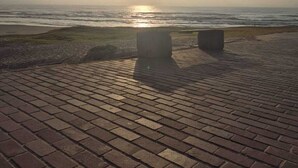 Un sendero pavimentado que conduce a la playa, con un banco y una estructura de piedra.