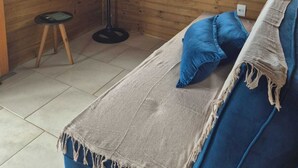 Una habitación con piso de madera, una cama, un televisor, un ventilador de pie y una ventana con vistas a árboles.