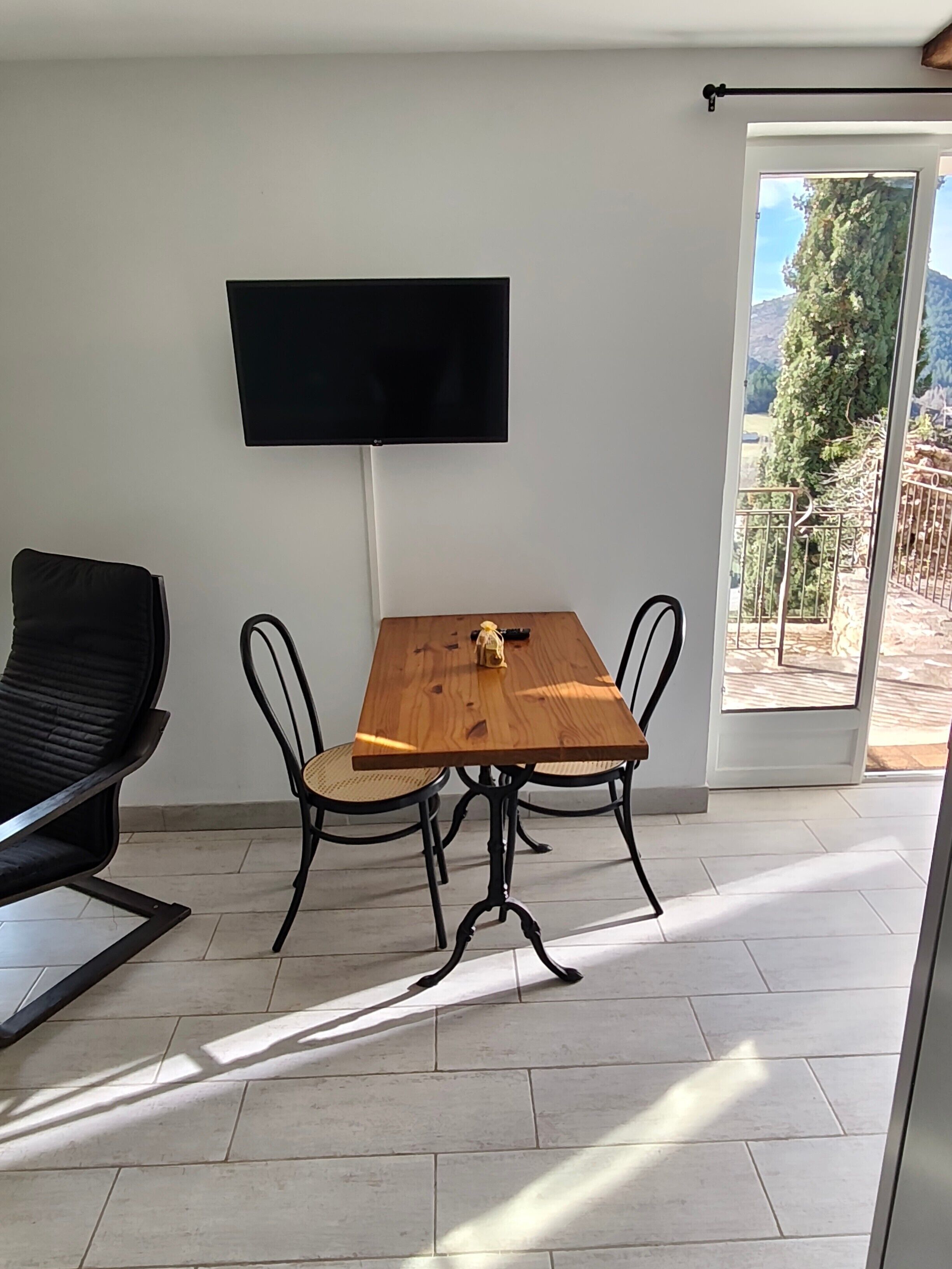 Ein Zimmer mit Holztisch, vier Stühlen, einer schwarzen Couch, einem flachbildfernseher an der Wand und einer Glastür, die zu einem Außenbereich führt.