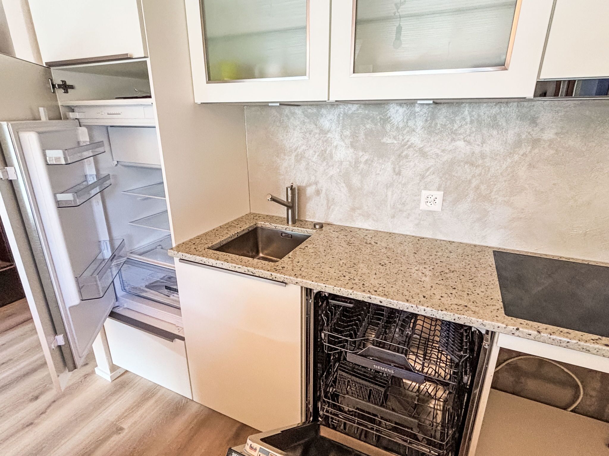 Una cocina compacta con armarios blancos, un lavamanos de acero inoxidable y un lavavajillas.