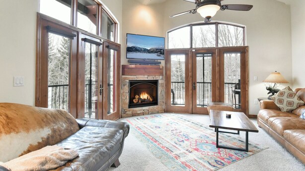 A cozy living room with a fireplace, leather sofas, a coffee table, and large windows offering a view of trees. - Marina Park Mountain View Townhome: Heart of Frisco (Frisco)