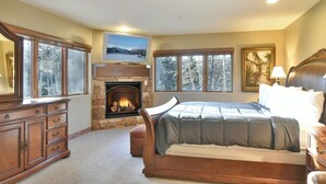 A bedroom with a stone fireplace, a large bed, a dresser, and a painting on the wall. - Marina Park Mountain View Townhome: Heart of Frisco (Frisco)