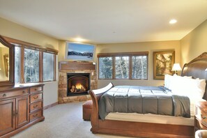 Ein Schlafzimmer mit Kamin aus Stein, einem großen Bett, einem Schminktisch und einem Gemälde an der Wand.