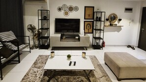 A modern living room with a flat-screen TV, a sofa, a coffee table, and a bookshelf. - premier luxury apartment (Accra)