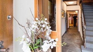 A hallway with a staircase, a wooden door, and a potted plant with white flowers.