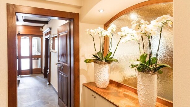 A hallway with a wooden door, a stone floor, and a wall-mounted mirror with white orchids.