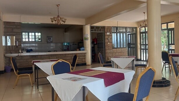 Un espace repas avec des tables et des chaises, une cuisine à l’arrière-plan et de grandes fenêtres.