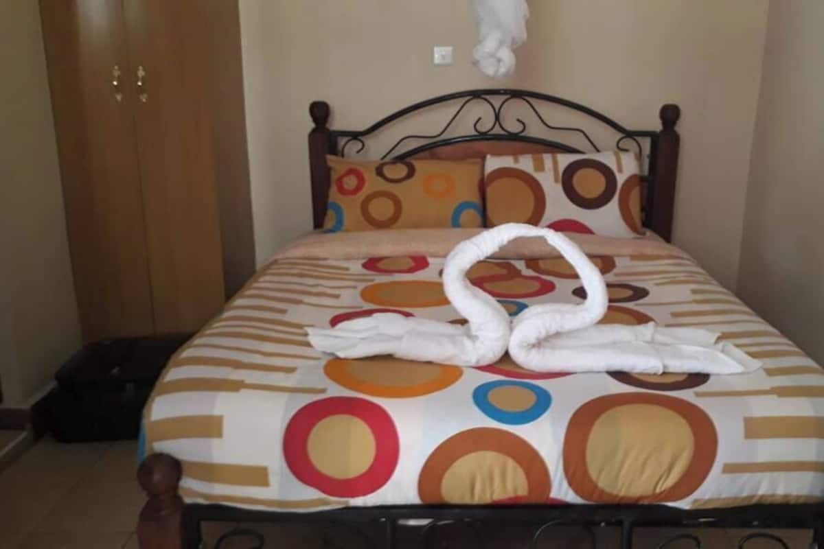 A bed with a patterned bedspread and two towels arranged in a swan shape.