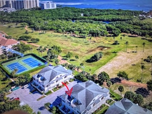 Vue aérienne d’un quartier résidentiel avec des maisons, un court de tennis et un grand parc verdoyant.
