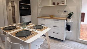 Una cocina moderna con armarios blancos, encimera de madera y una zona de comedor con platos, vasos y cubiertos.