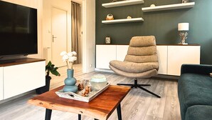 Una sala de estar moderna con un televisor de pantalla plana, una mesa de centro de madera con una bandeja, un sillón beige y un sofá verde oscuro.