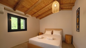 Ein Schlafzimmer mit Holzboden, einem Bett mit weißen Bettwäsche, zwei Nachttischen, einem Fenster und einem an der Wand hängenden Kunstwerk.