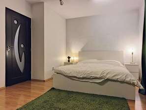 Un dormitorio con una cama, un tapete verde, una mesita de noche con una lámpara y una puerta con un diseño original.