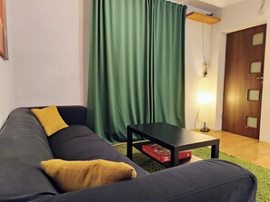 Una sala de estar con un sofá oscuro, una cortina verde, una mesita y una puerta de madera.