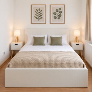 Una camera da letto con un letto, due comodini, due lampade, un termosifone e due stampe incorniciate a tema botanico.