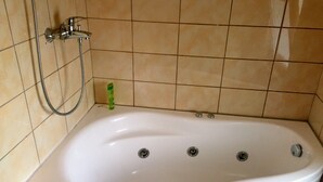 Een badkamer met een witte badkuip, een douchekop en een groene fles op de vloer.