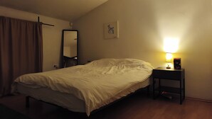 Een slaapkamer met een bed, een nachtkastje met een lamp, een spiegel en een wanddecoratie.