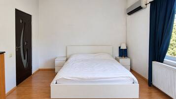 Een slaapkamer met een eenpersoonsbed, twee nachtkastjes, een raam met gordijnen en een airconditioning.