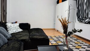Een moderne woonkamer met een zwarte bank, een glazen salontafel en een decoratieve vaas met gedroogde planten.