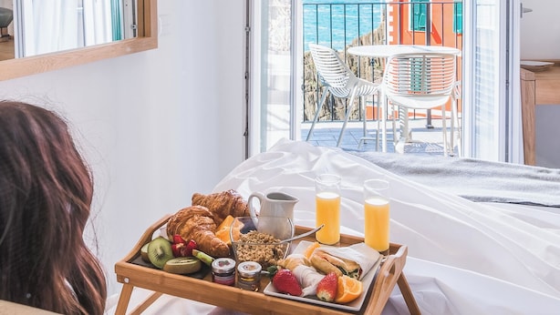 En balkong med ett brickbord för frukosten, utsikt över havet och en byggnad i orange och vita färger.