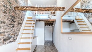En modern inredning med en trätrappa, en stenmur och en övre våningsplan med ett tak av synliga träbjälkar.