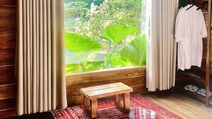 A room with wooden walls, a large window with curtains, a small wooden table, and a red patterned rug. - Wood Haven Homestay (Hoa Lu)