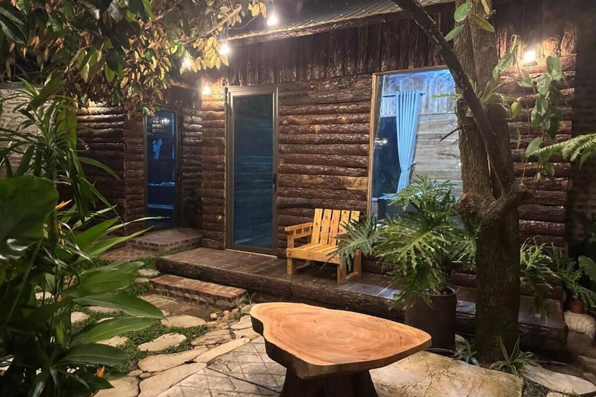 Une cabane rustique avec une façade en bois, un banc à l’extérieur et une table en pierre au premier plan.