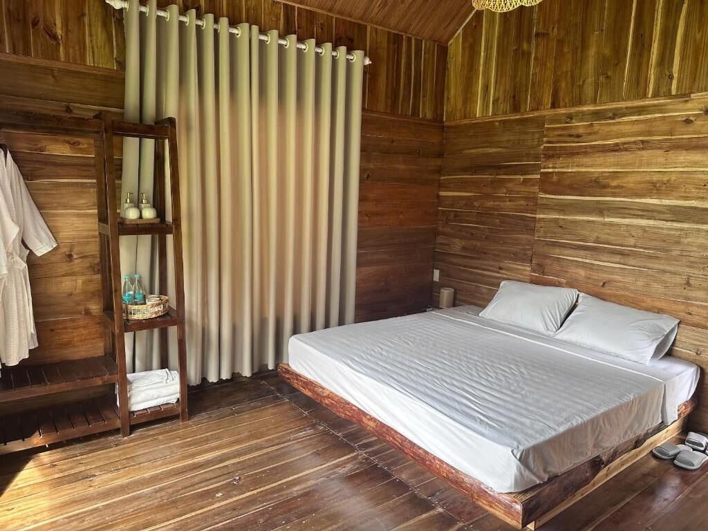 A wooden-paneled room with a bed, a shelf with toiletries, and a curtain.