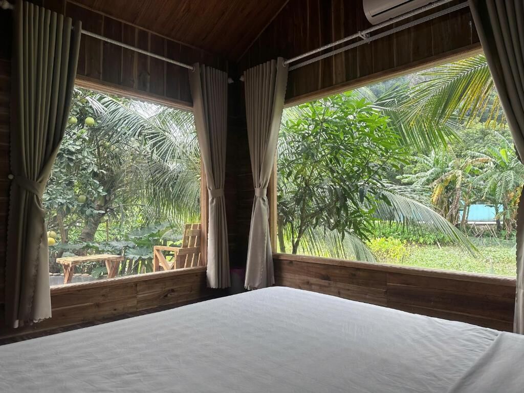 A room with a bed, wooden walls, and large windows overlooking a garden.