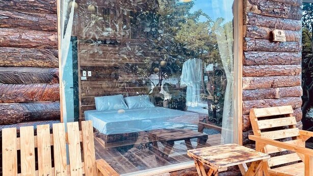 A log cabin room with a glass wall, a bed, wooden chairs, and a small table. - Wood Haven Homestay (Hoa Lu)