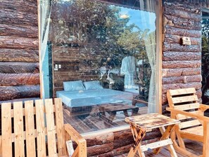 Une chambre aménagée dans un chalet en rondins, avec un mur en verre, un lit, des chaises en bois et une petite table.