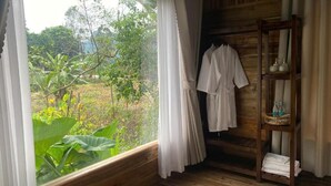 A wooden room with a large window, a wooden shelf with towels, and a view of greenery outside. - Wood Haven Homestay (Hoa Lu)