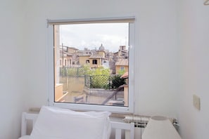 A room with a window overlooking a cityscape, a radiator, and a white bed. - Gorgeous penthouse with terrace near Piazza Navona (Roma)