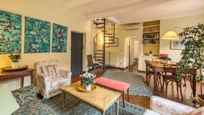 Un'ampia zona giorno con divano, poltrona e tavolo da pranzo. Una scala a chiocciola conduce a un piano superiore.