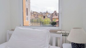 Una stanza con un letto, una finestra che si affaccia su edifici e una lampada.