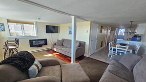 Een woonkamer met een bank, een televisie en een eethoek met een tafel en stoelen.
