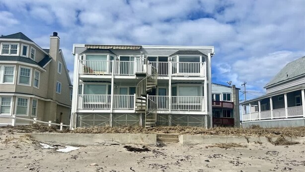 Een meerlaags gebouw aan het strand, met balkons en een spiraaltrap.