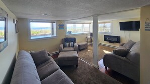 Een woonkamer met twee banken, een televisie en grote ramen met uitzicht op het strand.