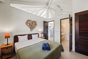 Une chambre d’hôtel avec un lit, une table de chevet, une lampe, un élément de décoration murale en forme de cœur et une vue sur la salle de bain par une porte ouverte.