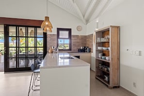 A modern kitchen with a central island, a wooden cabinet, and a view through a glass door. - NEW!!! Blue Bay Villa 13: Beautifully located with a view and close to the beach! (Willemstad)