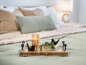 Ein Bett mit einem hölzernen Tablett, das eine Kerze, eine Vogelfigur und eine kleine Pflanze trägt.